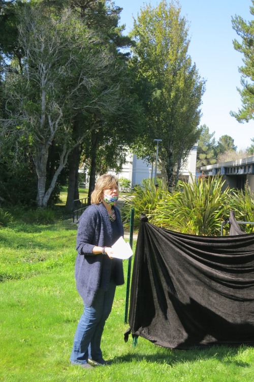 Dr. Patty Scott standing next to a shrouded tree before unveiling